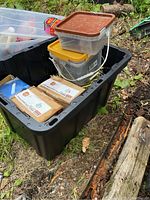 Photo of black 27 gallon plastic storage tote filled with construction supplies including boxes and containers.