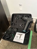 Opened carrying case showing the percussion massager, multiple head attachments, power adapter, and manual inside.