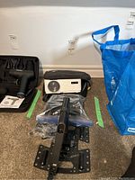 White Vankyo Leisure 470 projector with black carrying case, black metal mounts, and cables on carpeted floor