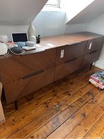 Side angled photo showing the dresser's wood grain and metal pulls with items on top.