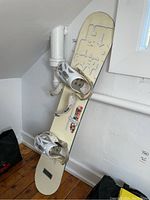Full view of the 61 inch cream-colored Salomon Prospect Ltd snowboard standing against the wall with white bindings attached.