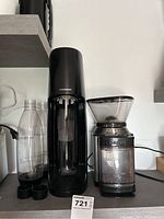 Black Sodastream sparkling water maker with two translucent bottles and black caps next to a Cuisinart coffee grinder; items placed on a kitchen countertop