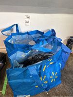 Two blue reusable Walmart bags holding strings of black corded lights with round Edison-style bulbs densely stored inside.