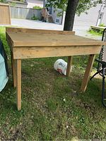 Full view of wooden work table outdoors on grass, showing top and legs.