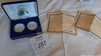 Photo of three silver coins in protective capsules displayed in blue velvet case alongside accompanying certificates of authenticity.