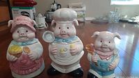Trio of pig canisters shown together on floor, each pig wearing distinct cooking-themed attire.