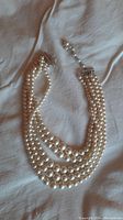 Five strand faux pearl necklace laid flat, showing the graduated sizes and clasp.