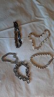 Five assorted silver chain bracelets of varied styles displayed on fabric.