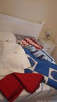 Lot of assorted blankets and quilts arranged on a bed, showing various quilt and knit afghan designs in red, white, and blue.
