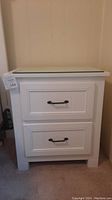 Full front view of the white nightstand showing two drawers and glass top protector.