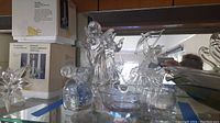 Shelf display of assorted glass and crystal figurines including angel, mouse, reindeer, bowls, and star-shaped ornament.