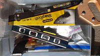 Top view of tools including Stanley Sharptooth handsaw in packaging, blue level, and various other tools and hardware inside clear plastic tote.