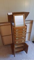 Front view of wooden standing jewelry box with open top mirror and drawers visible, also side panels with hooks for necklaces.