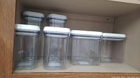 Set of seven OXO canisters arranged on a shelf: 2 tall, 4 medium, 1 wide canister.