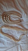 Pair of 4-strand faux pearl necklaces displayed side by side on fabric background.