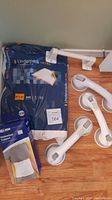 Items shown on wooden floor corner: four white suction grip safety handles, one large sealed pack of underpads, and one abdominal support band in original packaging.