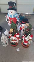Large and medium snowmen decorations including tall standalone snowmen with scarves and hats surrounded by smaller snowmen figures on decorated bases with Christmas trees and gift boxes.
