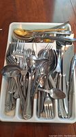 Photo of white tray filled with assorted forks, spoons, and knives with mixed handle designs.