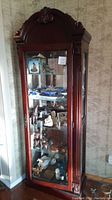 Full view of the dark wood Victorian-style curio cabinet with glass shelves and display items inside.
