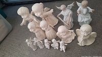 Overall collection of 11 white bisque porcelain angel figurines arranged on floor with various poses and sizes