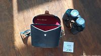 Opened leather case with red interior branding 'Sans & Streiffe', black binoculars next to it, and a lot card marked 230.