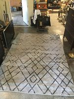 Full view of the rectangular grey area rug on concrete floor with diamond geometric pattern in darker grey lines.
