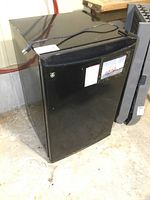 Black GE bar fridge showing front and side view with power cord on top.