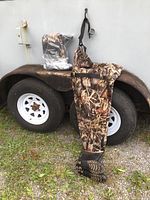 Two pairs of Night Cat chest waders with camouflage pattern and attached boots, displayed on trailer wheel. Boots size 45 (approx 11.5).