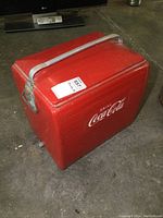 Main side view of vintage Coca Cola cooler showing red paint and white logo with metal handle on top.