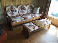 Wide shot showing the full sofa and coffee table set in a wood-paneled room, showcasing the cushions' woodland pattern and the heavy solid wood frames.