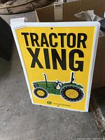 Full view of an embossed metal John Deere sign with yellow background, black 'TRACTOR XING' text, and green tractor graphic.