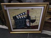Frontal view of framed canvas giclee print depicting Marilyn Monroe with movie clapperboard, wine bottle, wine glass, rose, in gold frame