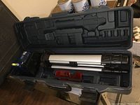 Open carrying case showing laser level, tripod, and mounting bracket.