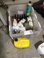 Overall view of a large plastic tote filled with various bottles of lubricants, oils, and other fluids. Includes a large yellow Karcher Deck Wash container outside the tote.