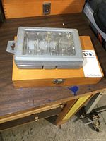 Gray plastic case of router bits on top of wooden case on workbench