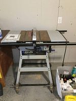 Front view of Delta 10-inch table saw with manual on table and wheeled base.
