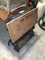 Folded Workmate 400 workbench showing wooden top with orange handle clamps and black folding metal legs.