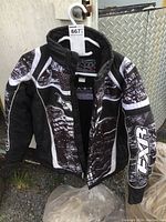 Front view of the black and white FXR youth race jacket hanging on a hanger.