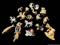 Full group photo of 17 vintage gold-tone figural brooches, pendant, and earrings on black background. Pieces depict various animals and figures including birds, fish, dog, owl, and cat.
