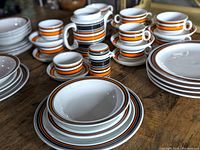 36-piece porcelain THOMAS 'SCANDIC' tableware set including cups, saucers, plates, teapot, sugar bowl, and creamer. Striped retro design in orange, black, brown.