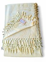 Folded view of the butter yellow jacquard table cloth showing intricate woven floral patterns and knotted fringed edges with the April Cornell tag attached.