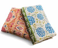 Two folded hand printed cotton tablecloths, one pink/peach and one blue/green, showing colors and patterns clearly.