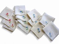 Twelve vintage handkerchiefs with various embroidered floral and bird patterns laid out showing details of designs and fabric.