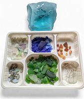 Overview of the lot showing the LG carved art glass paperweight and multiple compartments holding various colors of beach glass and silver wire pieces.