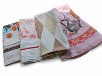 Four folded vintage table linens showing various designs including floral, geometric, and teapot motifs with different color schemes.