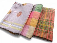 Photo showing three folded tablecloths with varied colorful patterns including florals, checks, and patchwork.