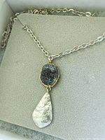 Close-up of the pendant necklace showing the brass-encased druzy quartz stone and hammered sterling silver teardrop on a chain laid in jewelry box.