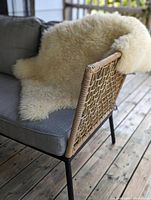 The sheepskin rug draped over a patio chair with woven backrest, showing its plush texture and natural cream color.