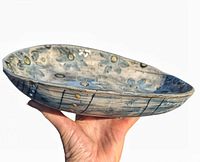 Side view of the asymmetrical footed pottery bowl showing blue daisy pattern on the interior and abstract pattern on the exterior with round feet supporting it.