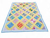Full view of quilt spread showing colorful diamond pattern with yellow borders and blue binding edge.